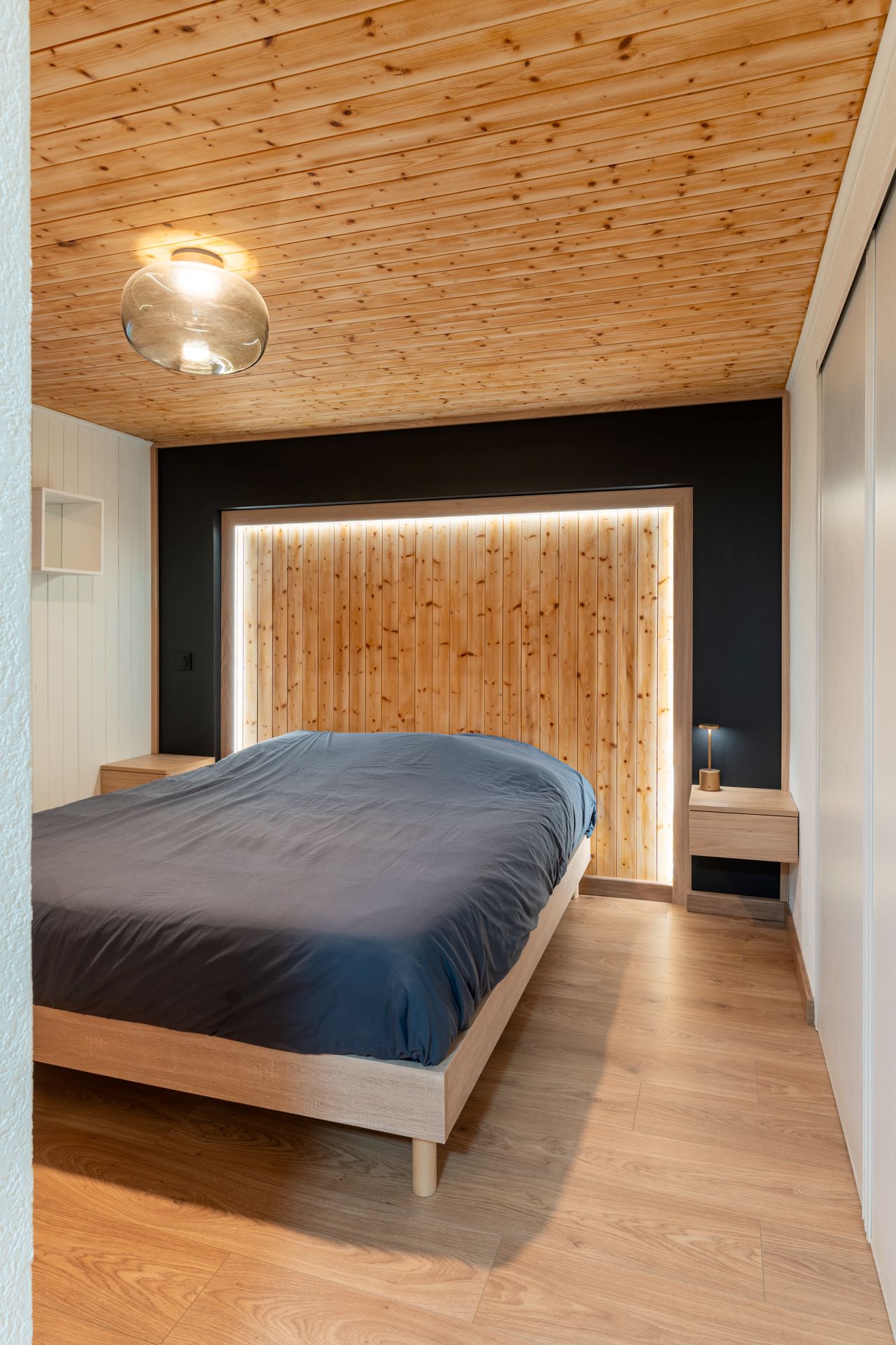 Chambre amis avec tête de lit bois éclairée, mur noir et ambiance moderne