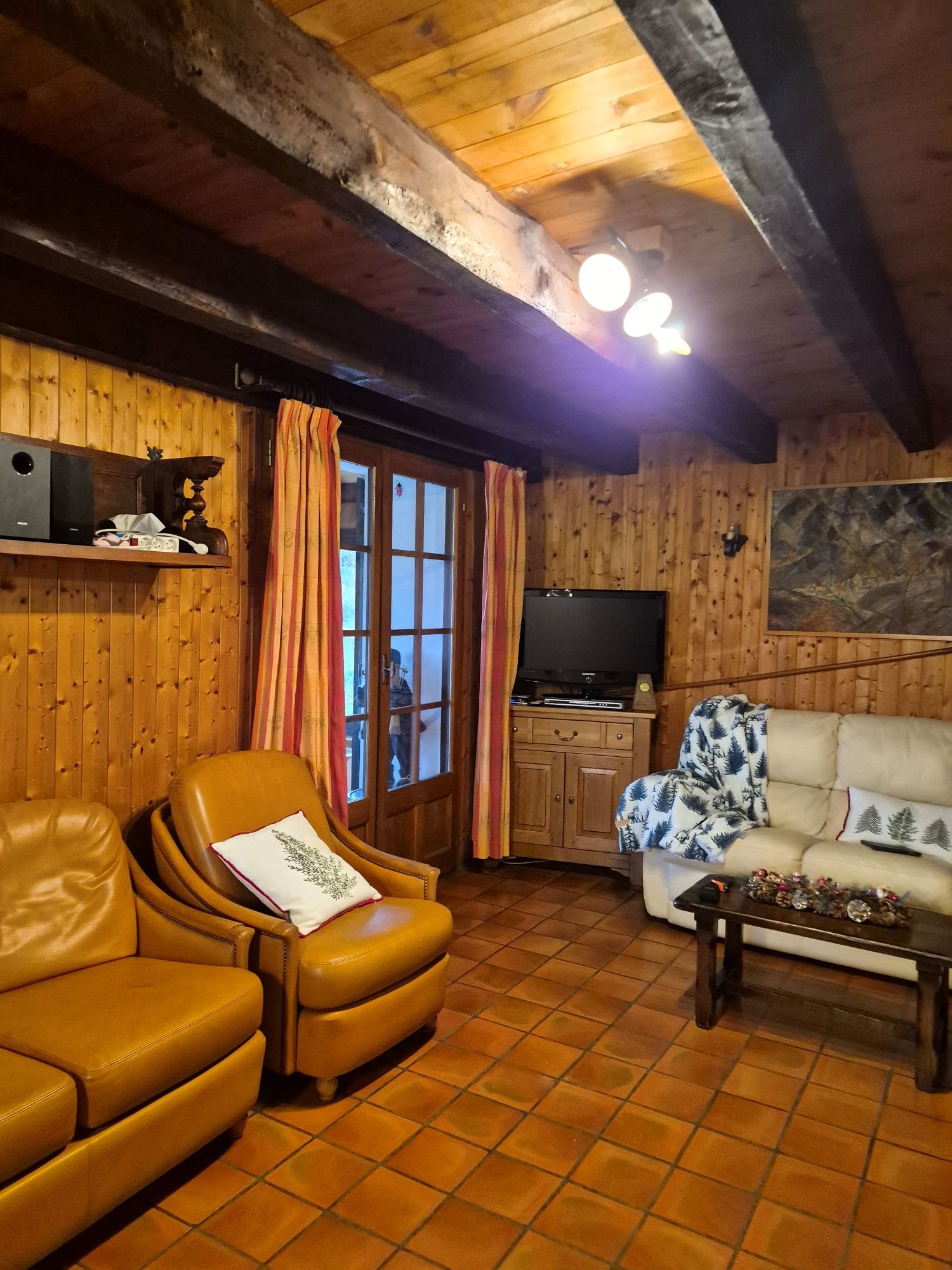 Salon avant rénovation avec lambris en bois foncé, poutres apparentes et sol en terre cuite